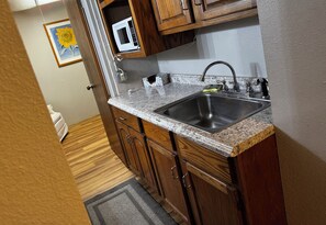 A kitchen with wooden cabinets, a granite countertop, a stainless steel sink, and a microwave.