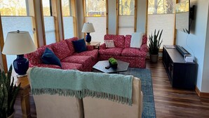 A living room with a red patterned sofa, a beige armchair, a green throw, a coffee table with a plant, and a TV on a stand. - Peaceful and Serene w/ Hot Tub and View (Eureka Springs)
