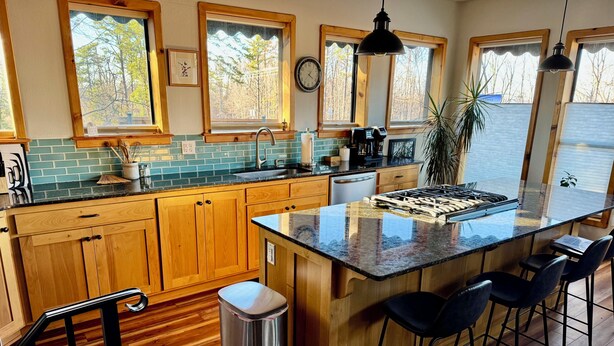 A kitchen with wooden cabinets, a granite countertop, a stainless steel trash can, and a bar area with stools. - Peaceful and Serene w/ Hot Tub and View (Eureka Springs)