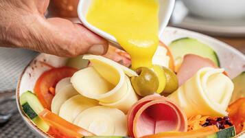 A bowl of assorted sliced vegetables and cheese with a hand pouring dressing over it.