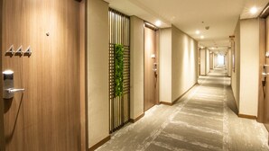 Un pasillo de hotel con puertas de madera, un jardín vertical verde y suelo alfombrado.