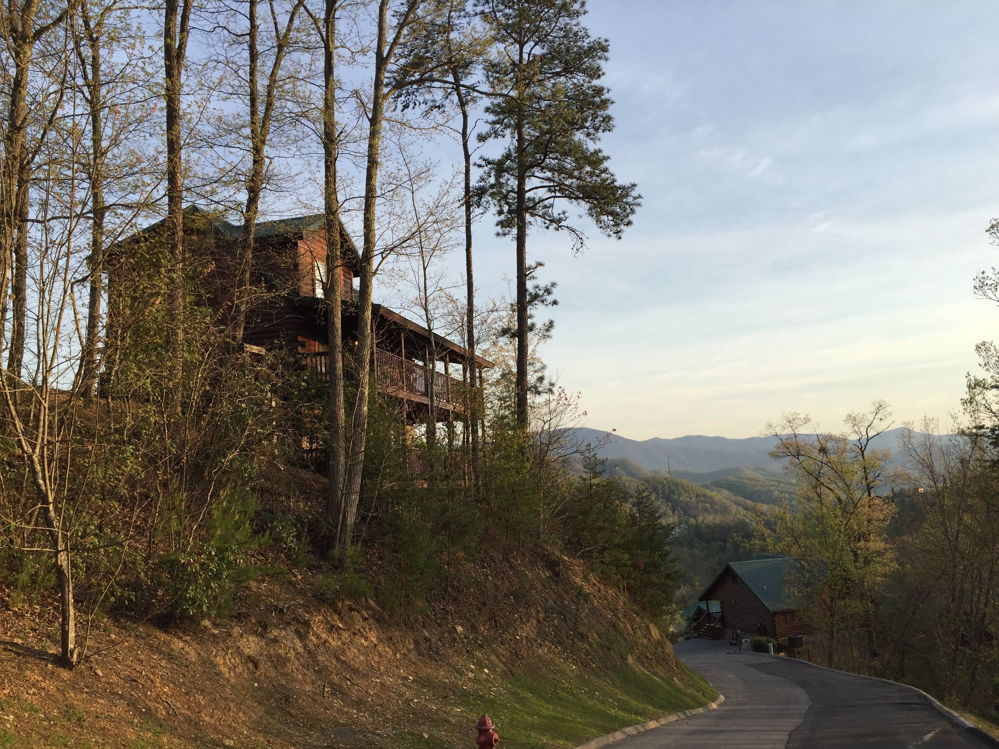 Eine Hütte mit einem Balkon mit Blick auf einen bewaldeten Bereich, eine kurvenreiche Straße und entfernte Berge.