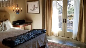 Ein Schlafzimmer mit einem großen Bett, einem Deckenventilator, einer Kristallleuchtre, einem gerahmten Bild und Blick durch eine Glastür in einen Außenbereich.