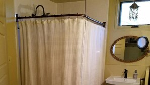 Ein Badezimmer mit Duschvorhang, Waschbecken, Spiegel und einem gemusterten Teppich.