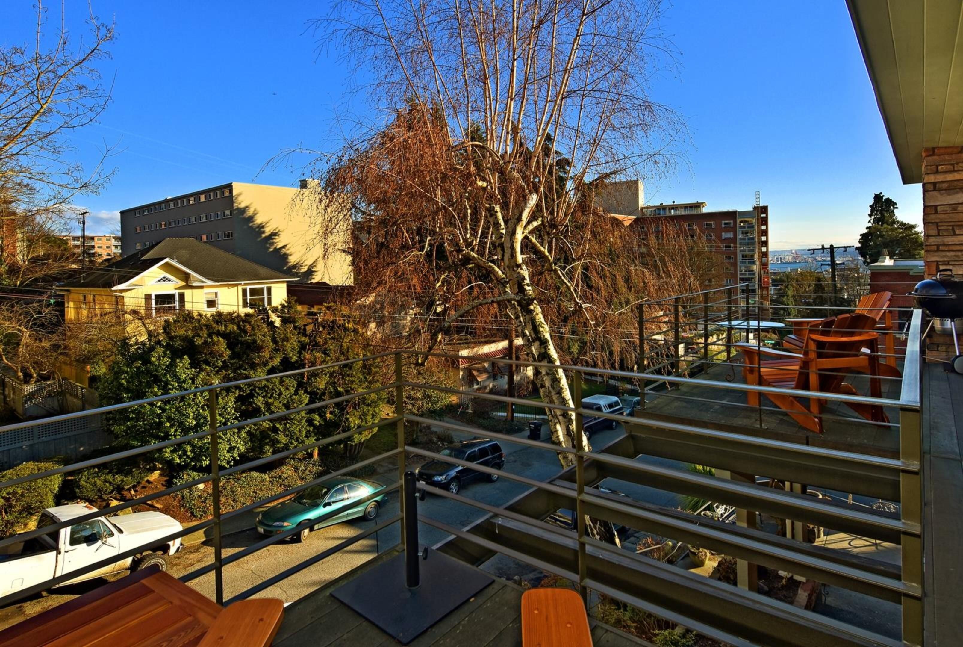 A balcony with a view of parked cars and buildings, a wooden table, and a metal railing.