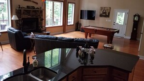 Un vaste salon doté d’une cheminée, d’une table de billard et d’une grande fenêtre donnant sur une terrasse.