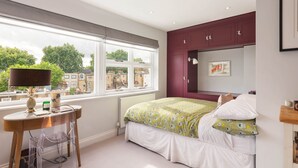 Une chambre à coucher avec un lit, une fenêtre, une table avec une lampe et un radiateur.