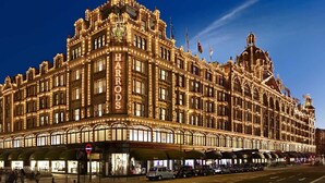 Un bâtiment imposant et richement décoré, portant en lettres bien visibles l’inscription « HARRODS », et se distinguant par ses éléments architecturaux classiques et son grand auvent d’entrée.