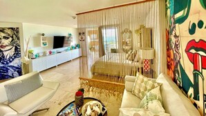 Een moderne woonkamer met een bank, een salontafel en een televisie. Achtergrond is een bed met hemel.