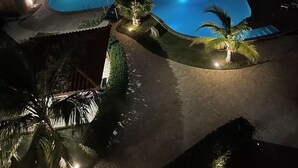 Een hotel met meerdere verdiepingen, een zwembadgedeelte, palmbomen en goed verlichte paden.