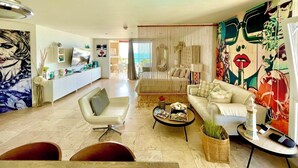 Een moderne woonkamer met een bank, fauteuil, salontafel en een eethoek, inclusief een televisie en decoratieve objecten.