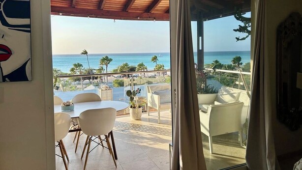 Een balkon met uitzicht op de oceaan, een eethoek met stoelen en een tafel, en een plafond met houten balken.