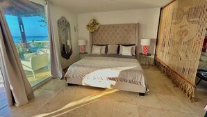 Een slaapkamer met een groot bed, uitzicht op zee en een balkon.