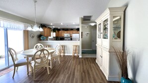 A kitchen with wooden cabinets, a dining table with chairs, and a blue vase with dried plants.
