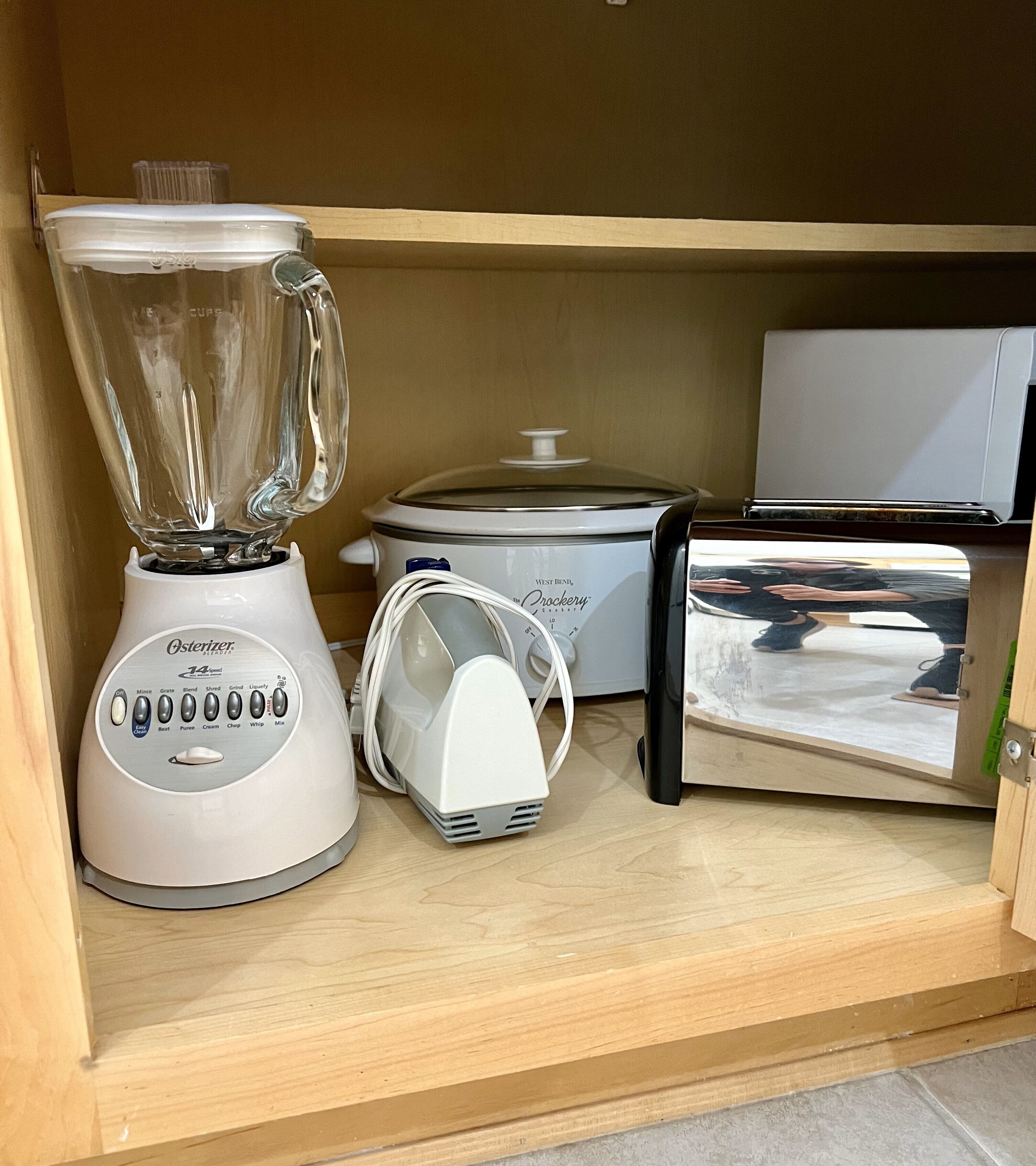A kitchen with a blender, toaster, and crockpot on a wooden shelf.