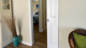 A hallway with a wooden floor leading to a bedroom with a bed and a painting on the wall.