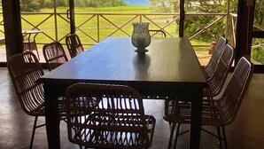 A dining area with a table and chairs, a vase, and a view of a green landscape through large windows. - Beach Front Home in Ballena Marine Natl Park (Uvita)