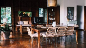 A dining area with a wooden table and wicker chairs, a television, and a bookshelf. - Beach Front Home in Ballena Marine Natl Park (Uvita)