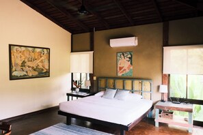 A bedroom with a bed, bedside tables, artwork, and an air conditioning unit.