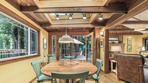 Un comedor con una mesa y sillas de madera, una lámpara colgante y vistas a un patio exterior a través de puertas de vidrio.
