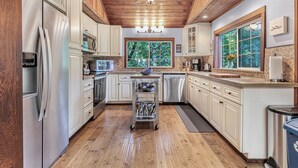 Una cocina moderna con electrodomésticos de acero inoxidable, techo de madera y un amplio ventanal con vistas al verdor.