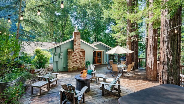 Una terraza de madera con asientos exteriores, una fogata y una chimenea de piedra.