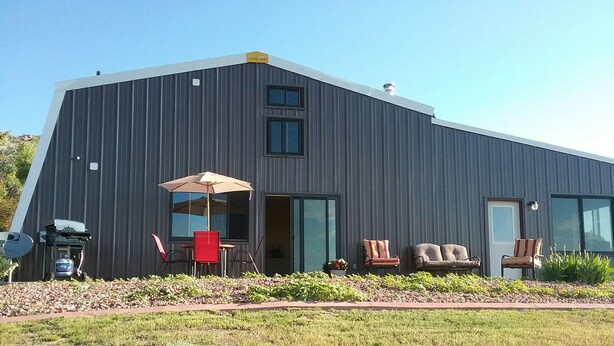 A modern building with a dark facade, large windows, and a patio area with outdoor furniture.
