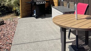 An outdoor patio with a round table, chairs, a grill, and a wooden fence.