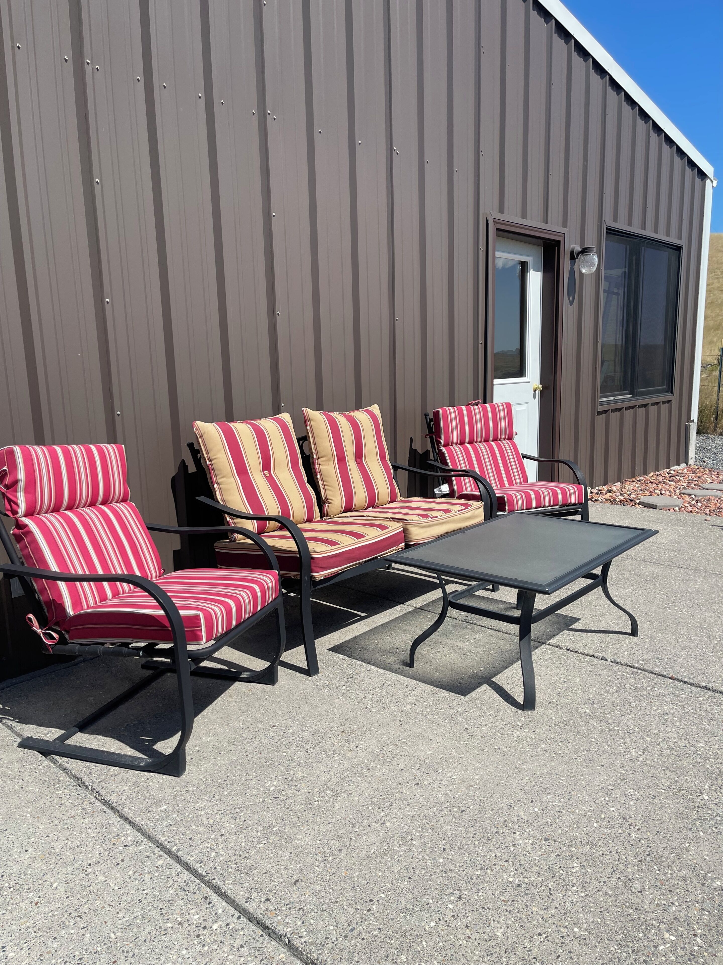 Une terrasse avec un ensemble de meubles de salon (canapé et fauteuils) et une table, une porte et une fenêtre.