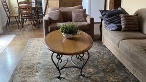 A living room with a round coffee table, two sofas, a dining table with chairs, and a kitchen area with wooden cabinets and a refrigerator.