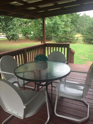 Een overdekt terras met een ronde glazen tafel en witte stoelen.