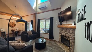 A modern living room with a fireplace, a flat-screen TV, a dining area with a wooden table and chairs, and a large clock on the wall. - ⛳️110 Golf Resort, 3 Bed 3 Bath, Sleeps 12, central A/C & private hot tub⛳️ (Kimberley)