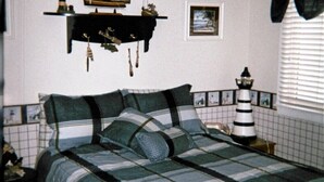 A bedroom with a bed, a wall-mounted ship model, a framed picture, and a nightstand with a lamp. - Waterfront Condo located on the shores of Lake Erie in Port Clinton, Ohio. (Port Clinton)