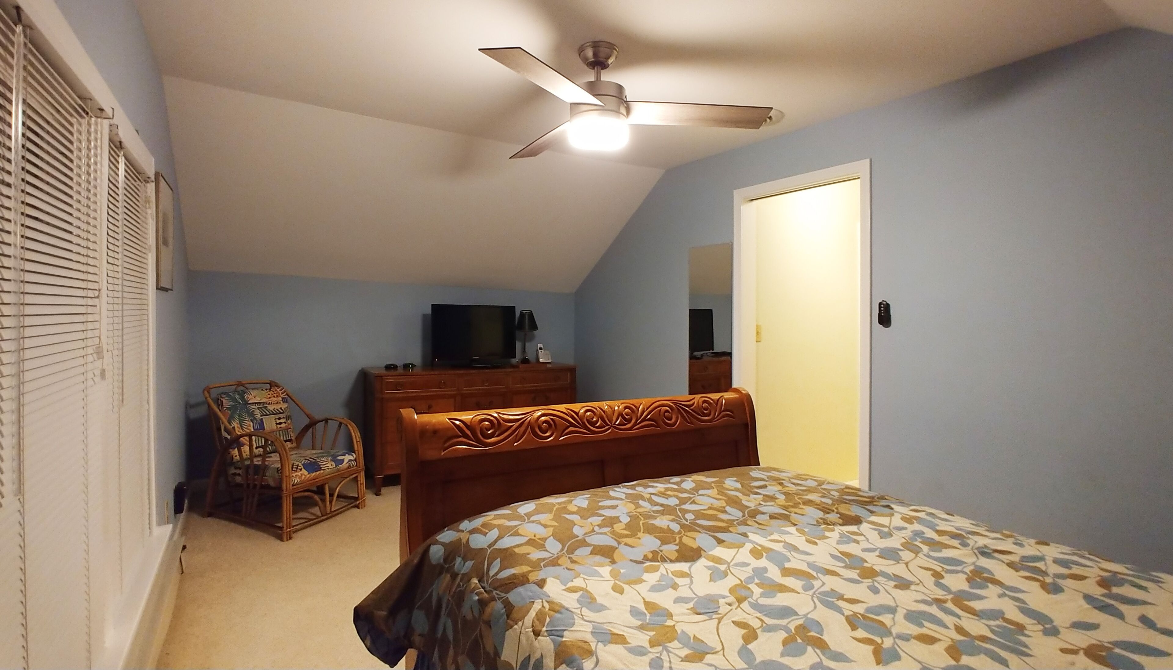 A bedroom with a bed, a dresser, a chair, a ceiling fan, and a television.