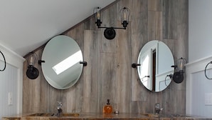 Et badeværelse med en trækommode, to runde spejle og en loftlampe.