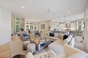 A spacious living room with a sofa, armchairs, and a coffee table. There is a kitchen area with a dining table and chairs.