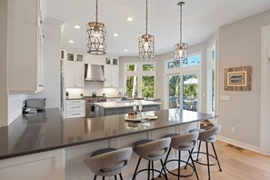 A modern kitchen with a large island, bar stools, pendant lighting, and a view of the outdoors.