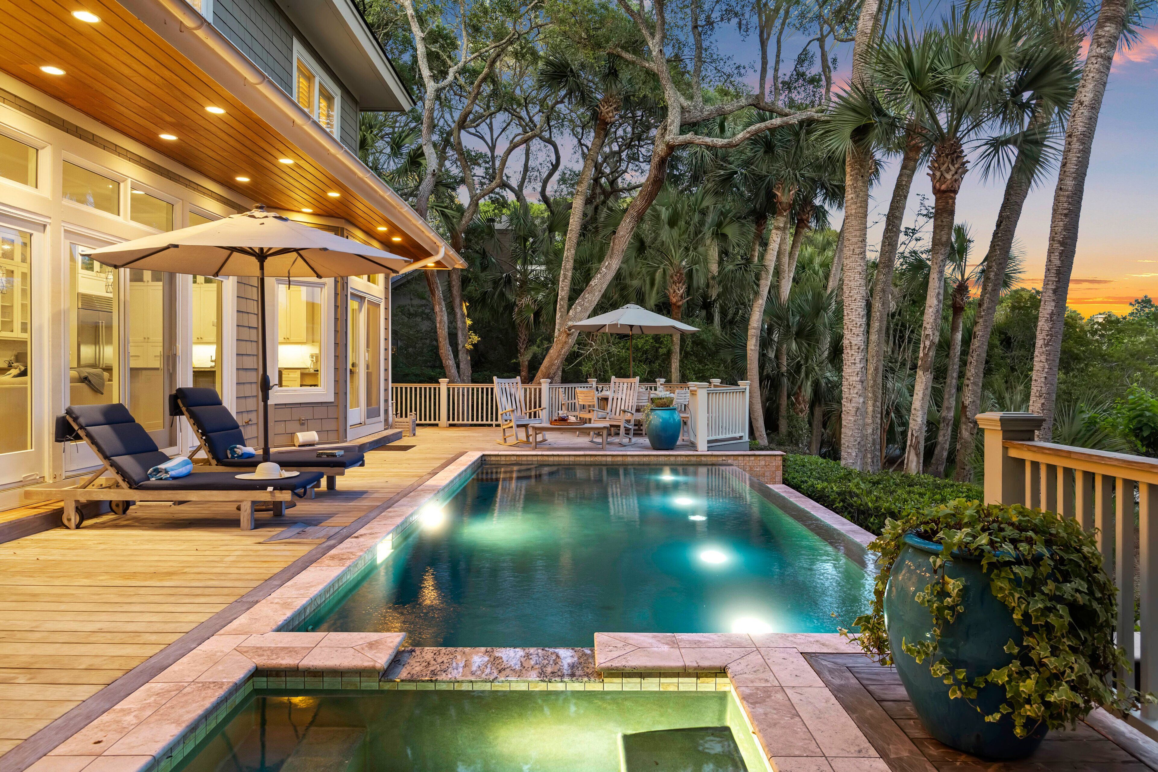 A swimming pool with lounge chairs and umbrellas, surrounded by trees and a wooden deck.