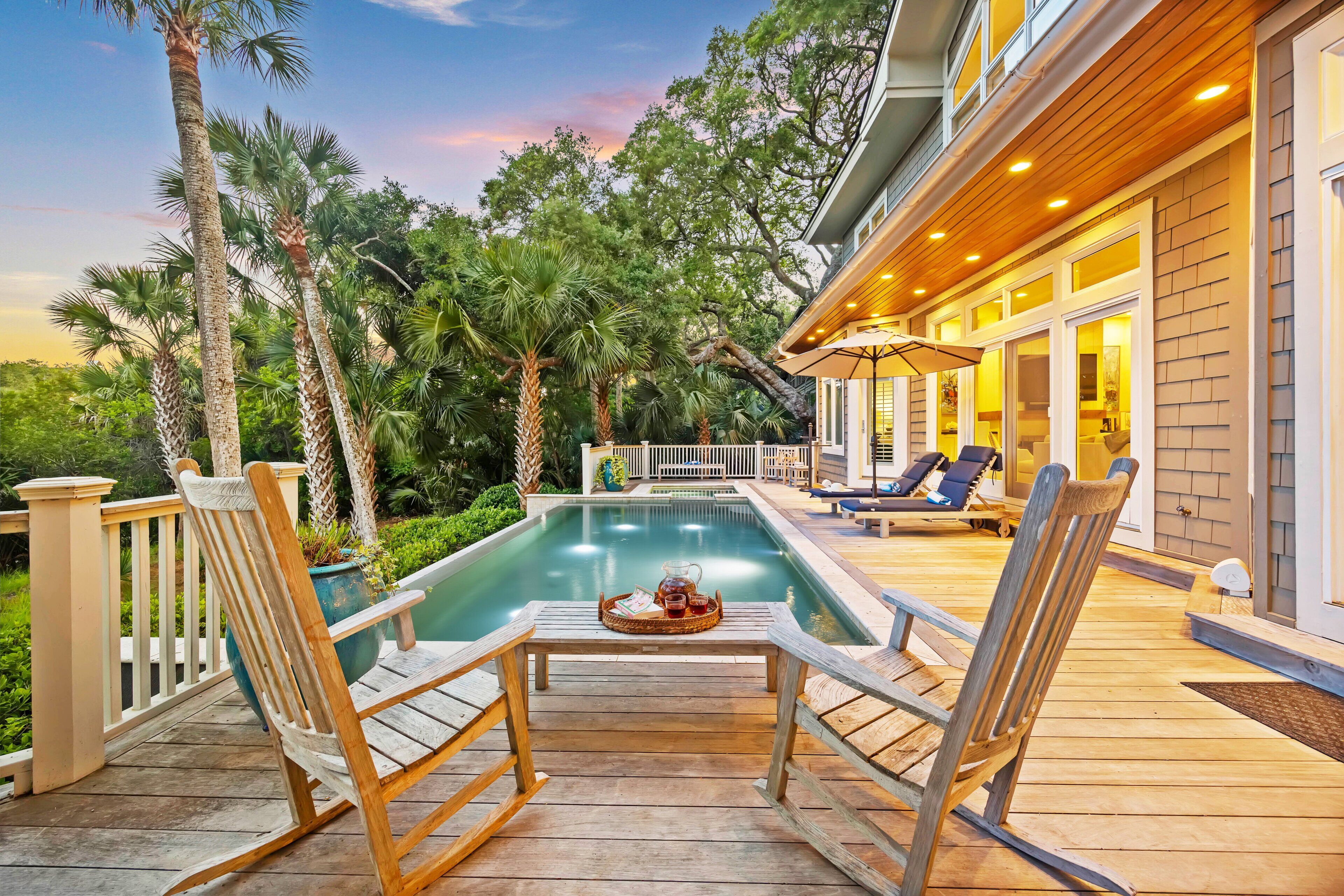 A wooden deck with a pool, lounge chairs, and a table with drinks.