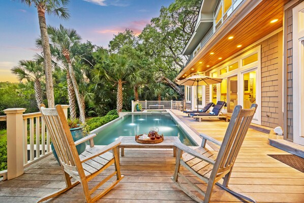 A wooden deck with a pool, lounge chairs, and a table with drinks.