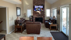 A spacious living room with a large sectional sofa, a fireplace, and a television mounted on a brick wall. - Ski Gunstock 3 minutes away then relax overlooking lakeWinnipesaukee







mile (GILFORD)