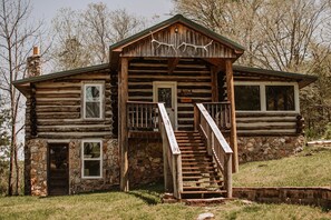 Eine rustikale Holzhütte mit Steinunterbau, einer Holztreppe und einer Veranda mit Geländer.