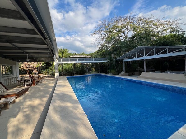 A swimming pool with a covered patio area, outdoor furniture, and a view of the surrounding greenery. - Outdoor Living in Absolute Privacy Steps from the Water's Edge (Playa Grande)