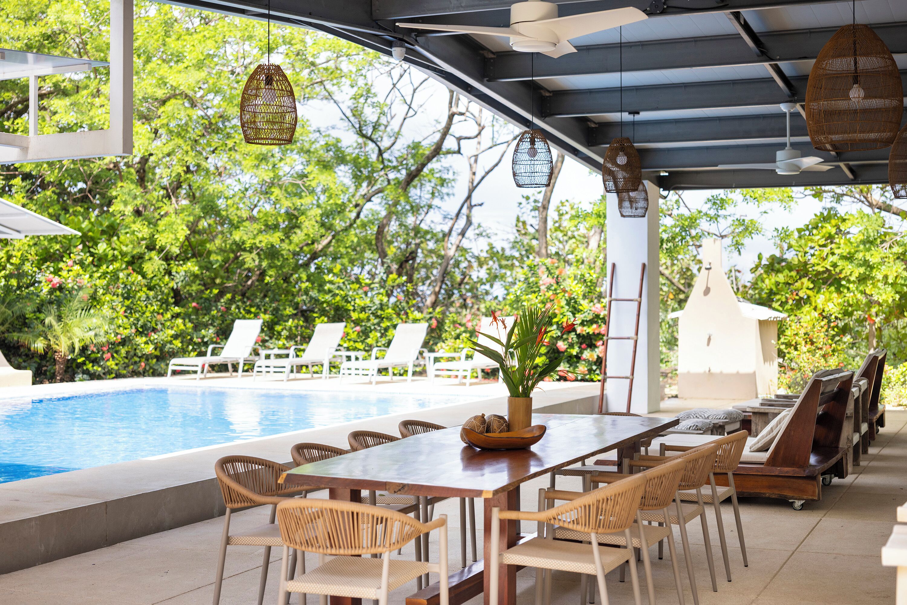 Un espace aménagé au bord de la piscine, avec une table en bois, des chaises en osier et un barbecue.