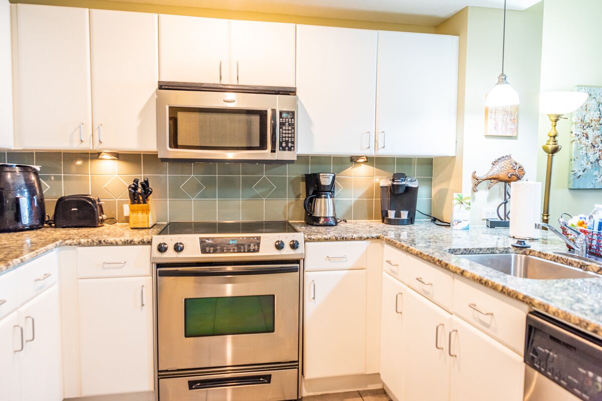 Een moderne keuken met witte kastjes, een roestvrijstalen magnetron, een fornuis en een vaatwasser.