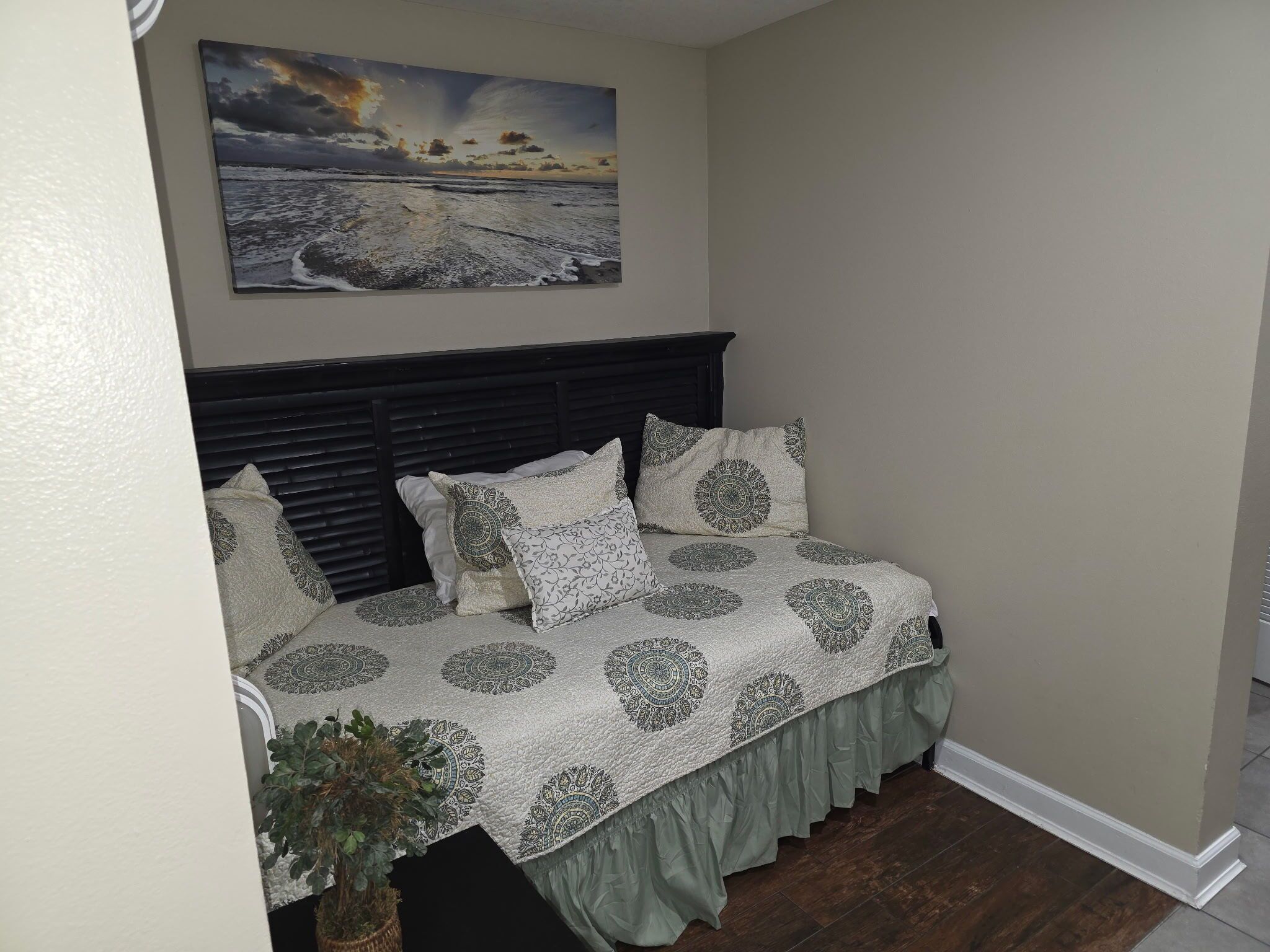 A bedroom with a bed, a headboard, a painting, and a potted plant.