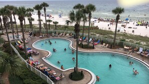 Un área de piscina con varias piscinas, rodeada de sillones de playa y sombrillas, con una playa al fondo.