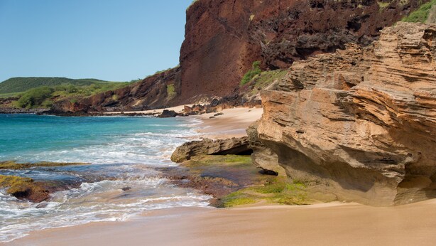 Paesaggio costiero con una formazione rocciosa evidente, spiaggia e oceano.