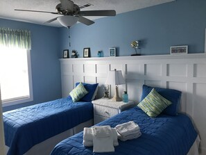 Two single beds with white headboard and bedside table, lamp, and decorative items.