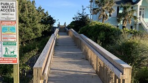 A wooden boardwalk leading to a house with a steep roof, surrounded by greenery and a clear sky. - 4 Bedroom, 2.5 Bath,  sleeps 8,  Ocean View, Large Family Room and Sunroom (Emerald Isle)
